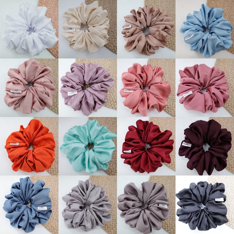 May include: A collection of 12 different colored satin scrunchies. The scrunchies are arranged in a grid pattern on a light brown background. Each scrunchie is made of a different color satin fabric, including white, beige, light brown, pink, purple, light blue, orange, turquoise, red, gray, dark gray, and blue.
