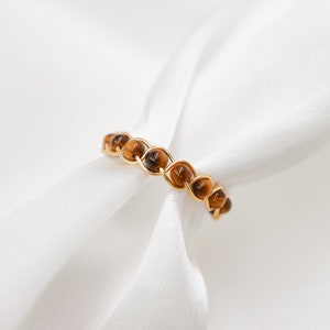 May include: A gold ring with a braided design featuring brown tiger's eye beads.