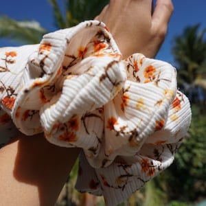May include: A white and orange floral patterned scrunchie made of fabric with a ribbed texture.