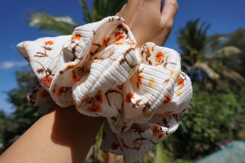 May include: A white and orange floral patterned scrunchie made of fabric with a ribbed texture.
