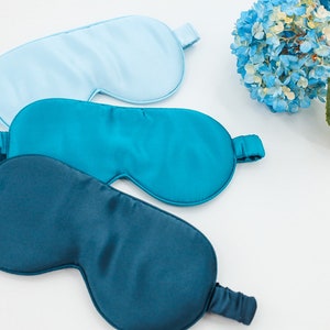May include: Three sleep masks made of soft, silky fabric. One mask is light blue, and the other two are shades of teal.