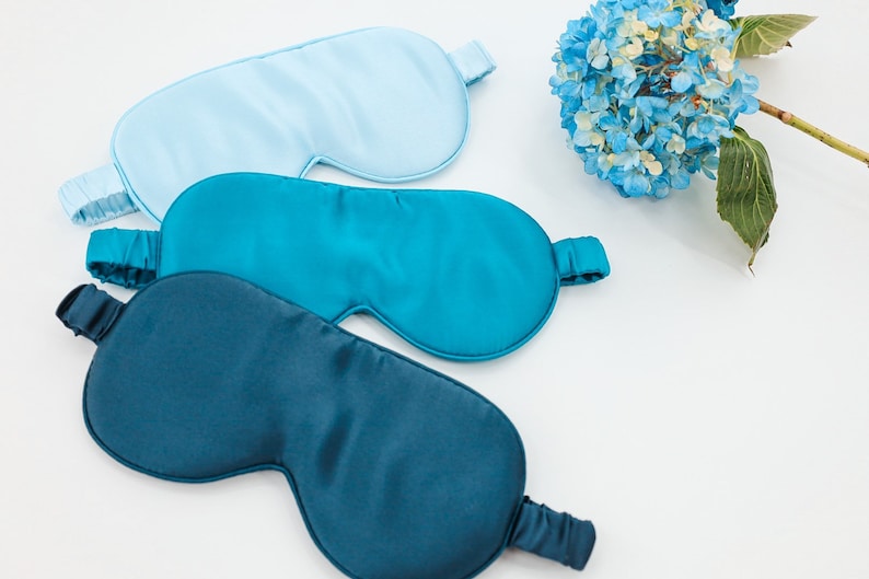 May include: Three sleep masks made of soft, silky fabric. One mask is light blue, and the other two are shades of teal.