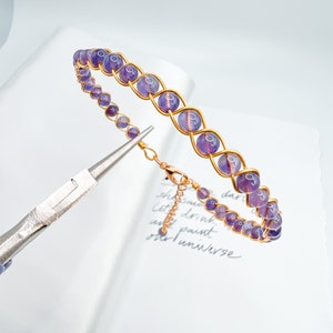 May include: A purple gemstone bracelet with gold wire wrapping. The bracelet has a clasp closure.