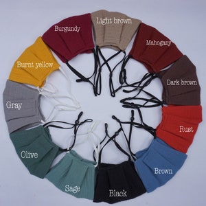 May include: A set of 12 face masks in various colors, including burnt yellow, gray, olive, sage, black, brown, rust, dark brown, mahogany, light brown, and burgundy. Each mask has a pleated design and adjustable straps.