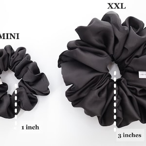 May include: Two black satin scrunchies, one measuring 1 inch in diameter and the other measuring 3 inches in diameter. The larger scrunchie has the text "Silk Creations Co." printed on it.