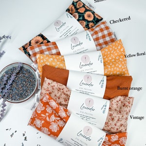 May include: Six eye pillows with different fabric patterns, including sunflower, checked, yellow floral, burnt orange, vintage, and orange floral. Each pillow is labelled "Lavender Eye Pillow" and filled with flax seed and organic lavender flowers.