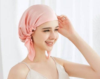 Op de afbeelding: Een roze satijnen slaapmuts met een strik aan de achterkant. De muts is ontworpen om haar te beschermen tegen breuk en pluis tijdens het slapen.
