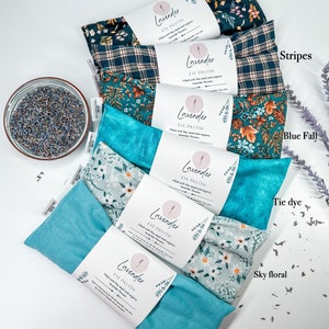 May include: A set of nine eye pillows with different fabric patterns. The pillows are labelled "Lavender Eye Pillow" and are filled with flax seed and organic lavender flowers. The patterns include navy floral, stripes, blue fall, tie dye, sky floral, and sky blue.