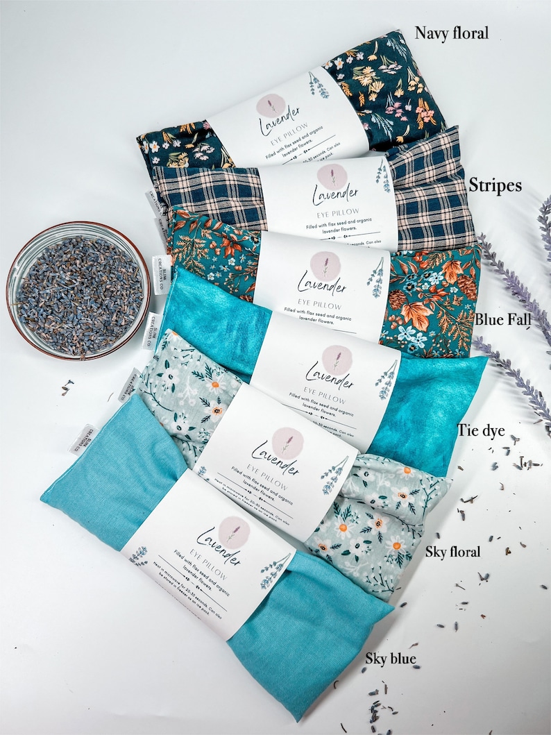 May include: A set of nine eye pillows with different fabric patterns. The pillows are labelled "Lavender Eye Pillow" and are filled with flax seed and organic lavender flowers. The patterns include navy floral, stripes, blue fall, tie dye, sky floral, and sky blue.