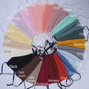 May include: A collection of pleated face masks in various colors, including pink, peach coral, and blue. Each mask has adjustable ear loops and is labeled with its color name, such as "Ivory," "Black," and "Rust."