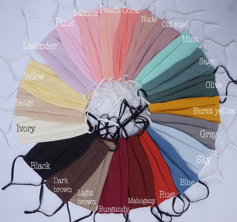 May include: A collection of pleated face masks in various colors, including pink, peach coral, and blue. Each mask has adjustable ear loops and is labeled with its color name, such as "Ivory," "Black," and "Rust."