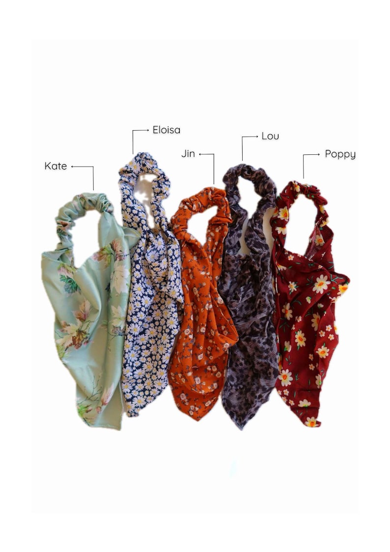 May include: Five colorful hair scrunchies with floral patterns. The scrunchies are arranged in a row from left to right: green with white flowers, blue with white flowers, orange with white flowers, purple with white flowers, and red with white flowers.
