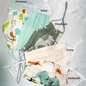 May include: Assortment of face masks in various colors and patterns. Designs include dinosaurs, elephants, and other animals. The masks have adjustable ear loops and are made of a soft, breathable fabric. The masks are labeled "Dinosaur", "Mint", "Elephant", "Ivory", and "Animals".