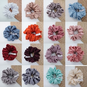 May include: Assortment of 12 colorful scrunchies made of soft fabric. The scrunchies are arranged in a grid pattern on a woven background.