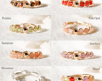 May include: A set of ten gold wire wrapped rings with different colored gemstones. The rings are arranged in two rows of five. The gemstones are: Tiger Eye, Carnelian, Peridot, Pink Opal, Sunstone, Amethyst, Moonstone, and Mixed.