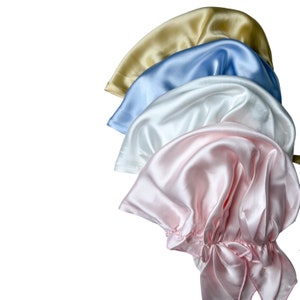 May include: Four satin sleep caps in different colors: beige, light blue, white, and pink. The pink cap is gathered at the bottom and tied with a bow.