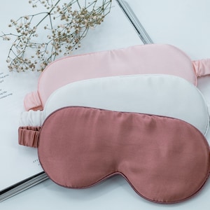 May include: Three silk sleep masks in pink, white, and rose colours. The masks are stacked on top of each other.