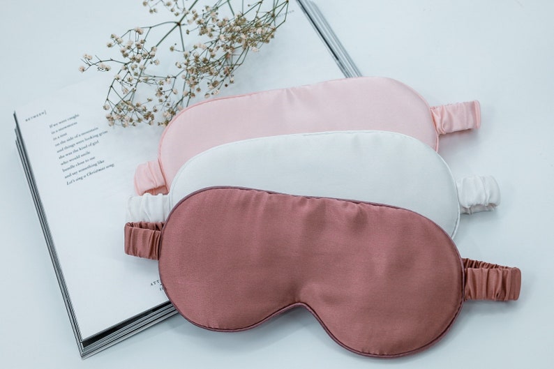 May include: Three silk sleep masks in pink, white, and rose colours. The masks are stacked on top of each other.