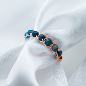 Può includere: Un delicato anello con un design a filo intrecciato e perline di pietre preziose blu.