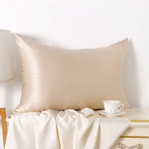 May include: A beige satin pillowcase on a white surface with a white teacup and saucer on the right side of the image.