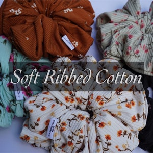 May include: Five soft ribbed cotton hair scrunchies in various floral patterns. The scrunchies are in the colors brown, green, white, and black.