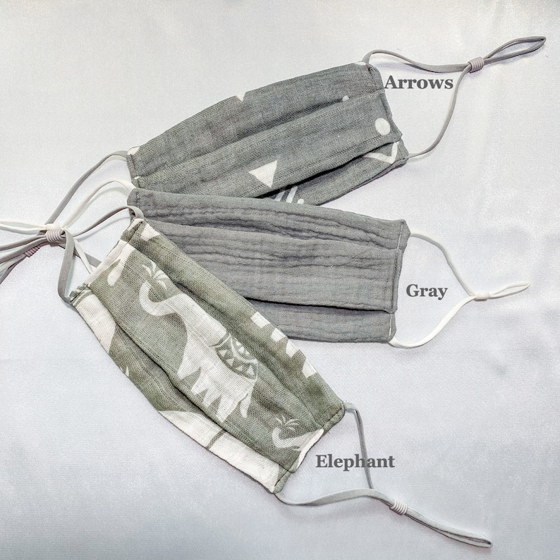 May include: Three face masks with adjustable ear loops are displayed. One is gray with white arrows and geometric shapes, another is solid gray, and the third is green and white with an elephant pattern. The text "Arrows", "Gray", and "Elephant" are visible.
