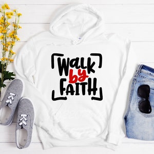 以下が含まれることがあります： 「Walk by Faith」という文字が太字の手書きのフォントで書かれた黒と赤のグラフィックが施された白いパーカー
