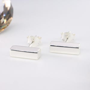 May include: A pair of silver bar stud earrings. The earrings are simple and minimalist, with a rectangular bar shape.