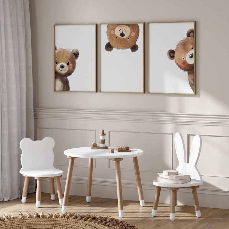 May include: A white wooden table and two chairs in a child's playroom. The table has a round top and four legs. The chairs are shaped like a bear and a bunny. There are three framed prints on the wall behind the table, each featuring a cartoon bear.