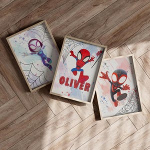 May include: Three framed prints with a watercolor background and black spiderwebs. The prints feature cartoon versions of Spider-Man in different poses. One print has the name "Oliver" written in red letters.