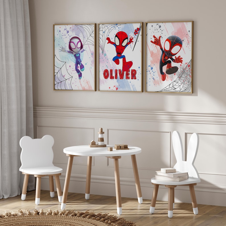 May include: Three framed prints of cartoon superheroes with a white background and colorful watercolor splatters. The prints feature a red and blue Spiderman, a black and red Spiderman, and a purple and blue Spiderman. The middle print has the name "Oliver" written in red letters.