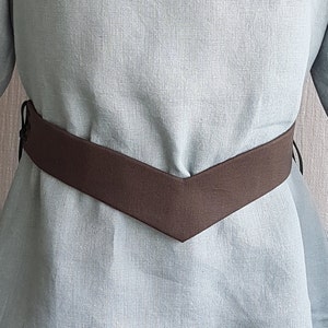 May include: A light blue linen shirt with a brown V-shaped belt.