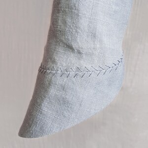 May include: A close-up of a gray linen fabric with a stitched seam around the edge. The fabric is folded and the seam is visible.