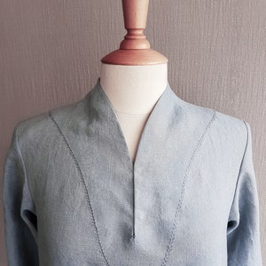 May include: A light blue linen shirt with a V-neck and decorative stitching on the neckline.
