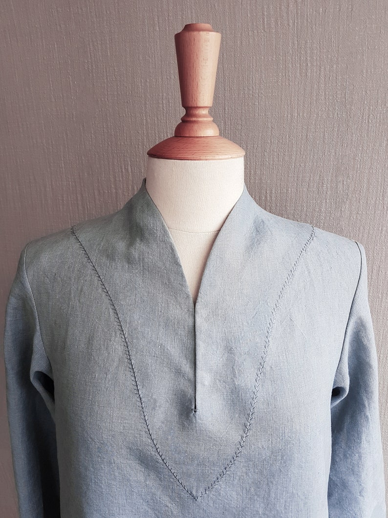May include: A light blue linen shirt with a V-neck and decorative stitching on the neckline.