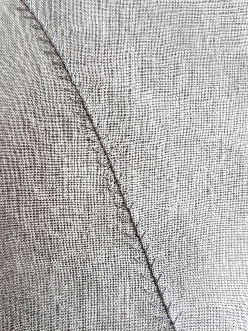 May include: Close-up of a gray fabric with a diagonal stitch line.