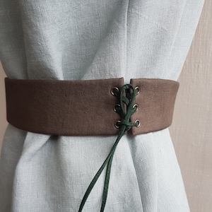May include: A brown fabric belt with a green lace-up detail. The belt is tied at the front and has metal eyelets.