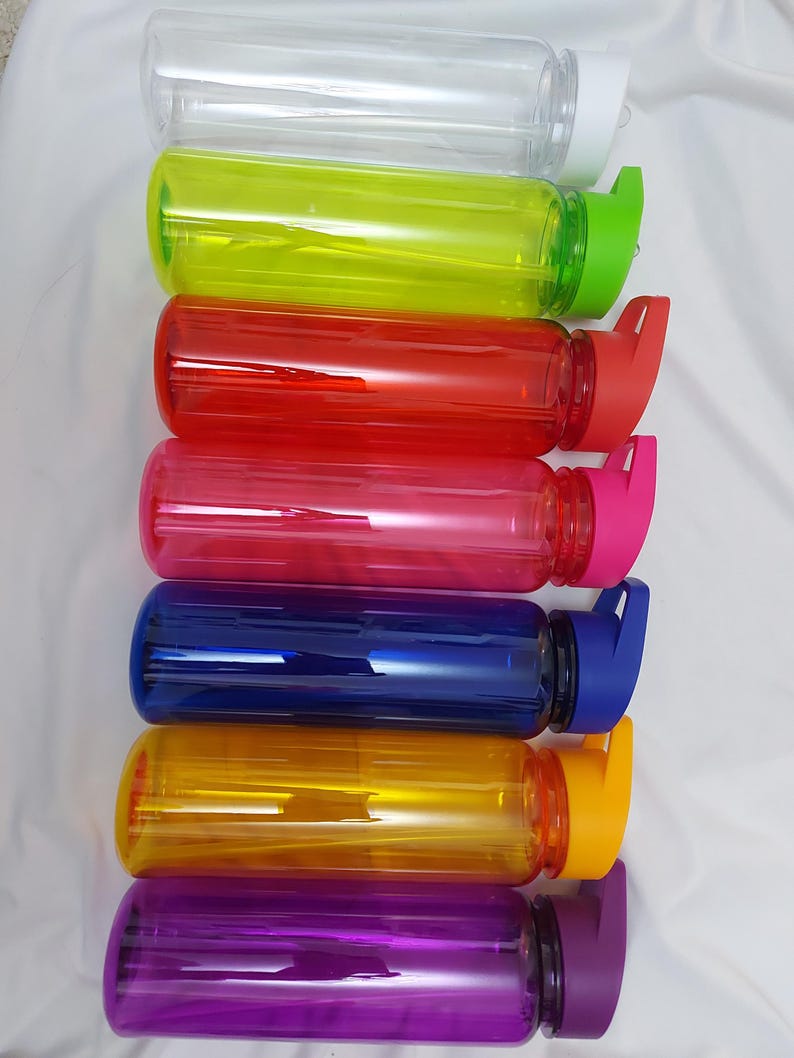 Puede incluir: Conjunto de siete botellas de agua de pl&aacute;stico transparente con tapas de diferentes colores. Las tapas tienen un dise&ntilde;o de tapa abatible. Las botellas est&aacute;n dispuestas en una pila vertical de arriba a abajo: transparente, amarilla, roja, rosa, azul, naranja y morada.