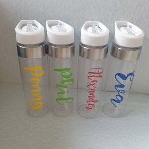 Puede incluir: Cuatro botellas de agua de pl&aacute;stico transparente con detalles de acero inoxidable y nombres personalizados. Los nombres son "Penny", "Rohit", "Alexander" y "Enya".