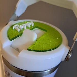 May include: White travel mug with a green lid and a handle. The lid has a green glitter finish and the words "Pepin" are printed on the lid. The mug has the word "Allstars" printed on the side.