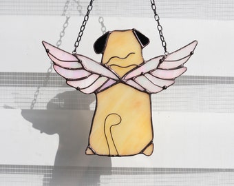May include: A stained glass window hanging with a beige pug with pink wings. The pug is facing away from the viewer and has its tail curled up.