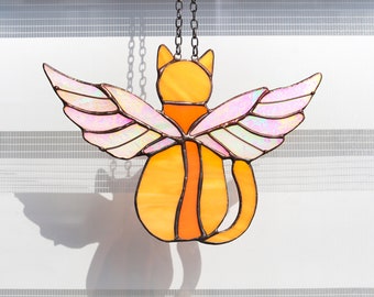 May include: A stained glass cat with iridescent wings hanging from a chain. The cat is orange and the wings are pink.