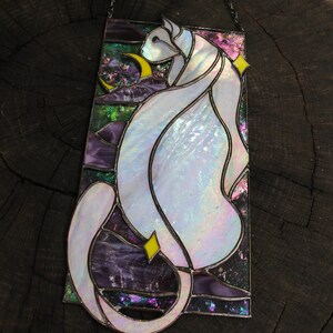 May include: A stained glass window hanging from a chain, featuring a white cat with iridescent glass, sitting with a crescent moon and stars in the background.