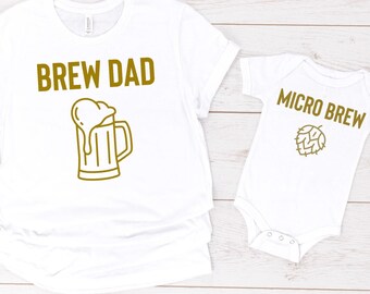 Könnte beinhalten: Weißes T-Shirt mit dem Text "Brew Dad" und einer Grafik eines Bierkruges mit Schaum. Weißer Baby-Strampler mit dem Text "Micro Brew" und einer Grafik einer Hopfenpflanze.