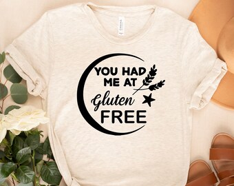 Könnte beinhalten: Ein beiges T-Shirt mit dem Text "You had me at gluten free" in einem schwarzen Kreis mit einem Weizenähren-Design.