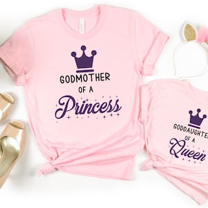 May include: Two pink t-shirts with a purple crown and text. The larger shirt says "Godmother of a Princess" and the smaller shirt says "Goddaughter of a Queen".