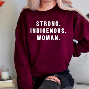 Puede incluir: Sudadera color burdeos con el texto "STRONG. INDIGENOUS. WOMAN." impreso en blanco.