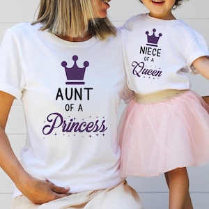 May include: Two white t-shirts with purple crowns and text. The larger shirt says "Aunt of a Princess" and the smaller shirt says "Niece of a Queen".