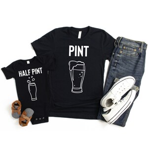 以下が含まれることがあります： 「PINT」という文字と白いビールグラスのアウトラインが描かれた黒いTシャツ。 「HALF PINT」という文字と白い小さなビールグラスのアウトラインが描かれた黒いロンパース。