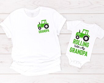 May include: White t-shirt and onesie set with green tractor graphics. The t-shirt has the word "GRANDPA" below the tractor. The onesie says "ROLLING WITH MY GRANDPA".